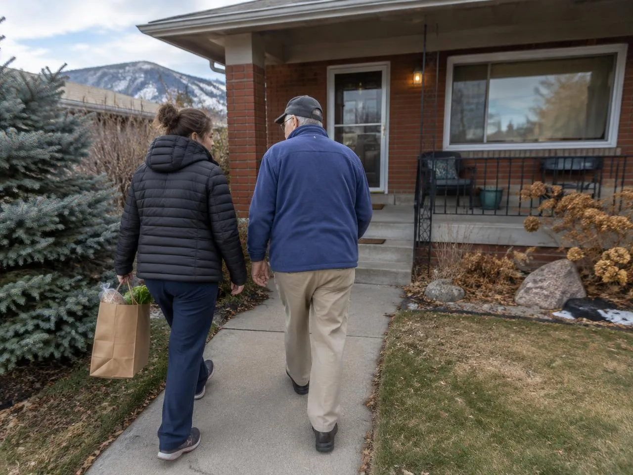 Caregiver carrying groceries up the front walk with a senior man in Englewood